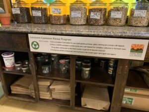 A variety of bulk containers with different nuts and other goods with a Locavore Container Reuse Sign below it