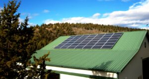 A green rooftop of a shop building with solar panels on top and a hill in the background