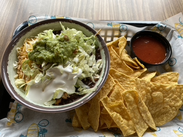 A tray of food featuring chips and salsa and mexican food in a ceramic reusable bowl