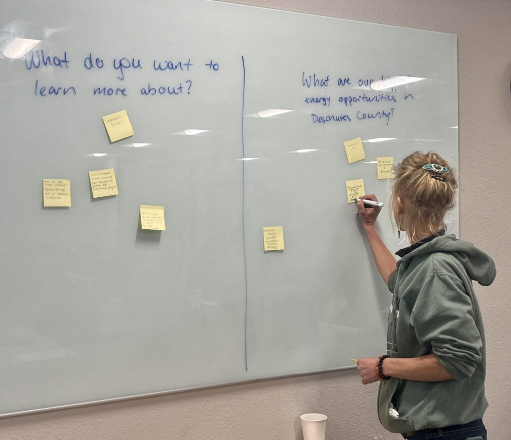 a person with blonde hair wearing a hoodie writes on sticky notes on a whiteboard