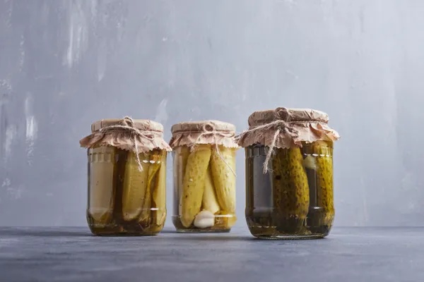 Pickled cucumbers in glass jars on blue background.