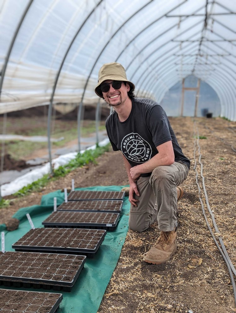 Young farmer with hat next to seeding trays in a greenhouse