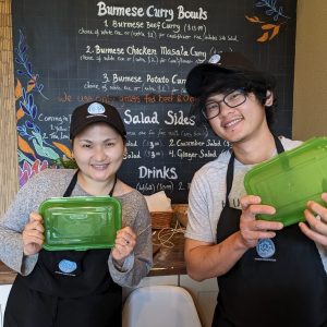 Pic of two employees at an eatery showing off green Rogue To Go takeout containers