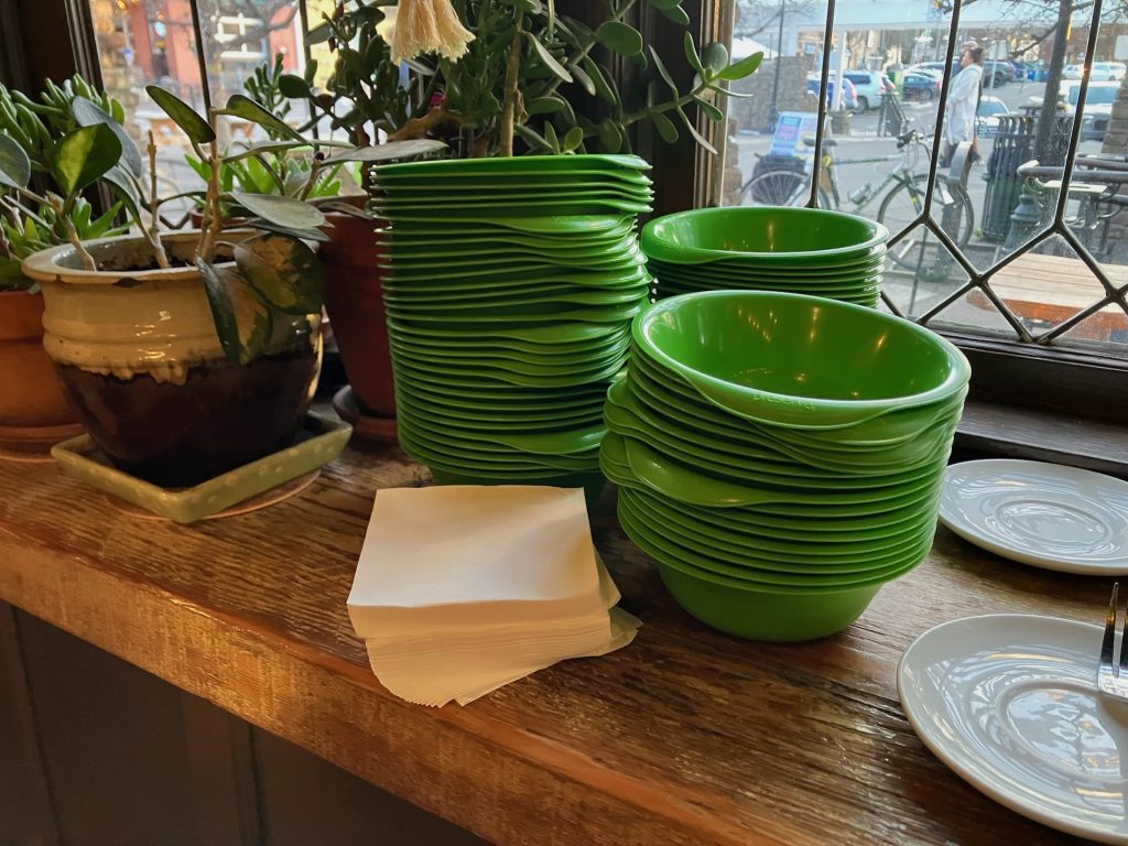 Stacks of green reusable plastic bowls on a wooden counter in front of a window