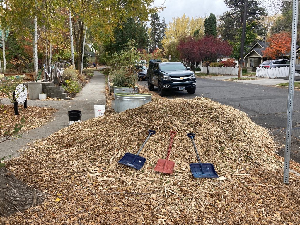 a pile of woodchips in front of a building with three shovels in front of the pile