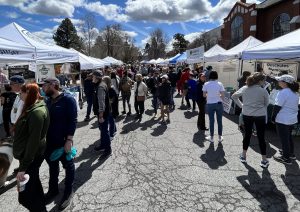 Street with vendor tents and people walking, under a blue sky with clouds.