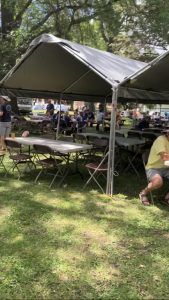 Some tables and chairs on grass under canopies with few folks around