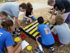 Several young people painting a pallet board with colors.