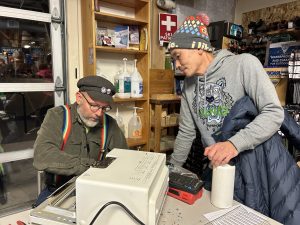 volunteer fixer with hat and colorful suspenders helps fix attendee's item