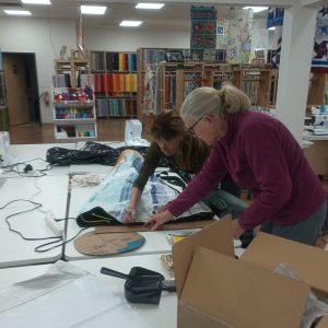 two people measuring or working with vinyl on a large craft table