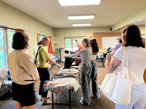 People sifting through piles of clothes organized on tables in a big room