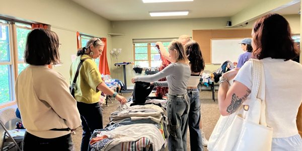 People sifting through piles of clothes organized on tables in a big room