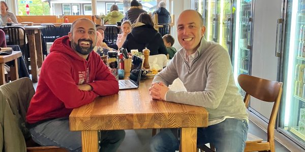 Two men sitting across from each other at a table in a restaurant looking at the camera smiling