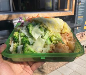 Fried rice in a green reusable clamshell container in front of a food cart window