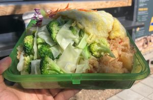 Fried rice in a green reusable clamshell container in front of a food cart window