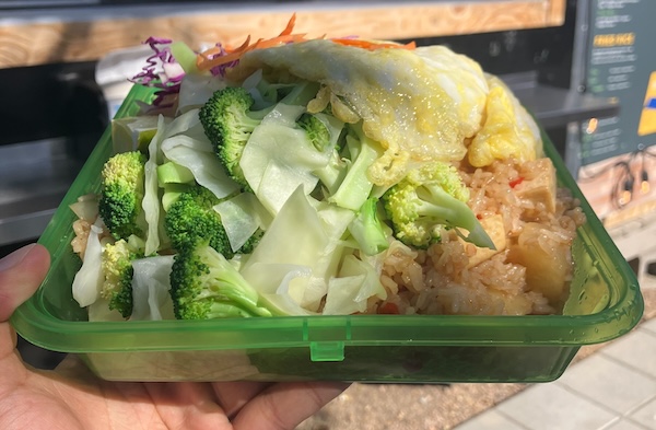 Fried rice in a green reusable clamshell container in front of a food cart window