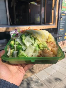 Fried rice in a green reusable clamshell container in front of a food cart window