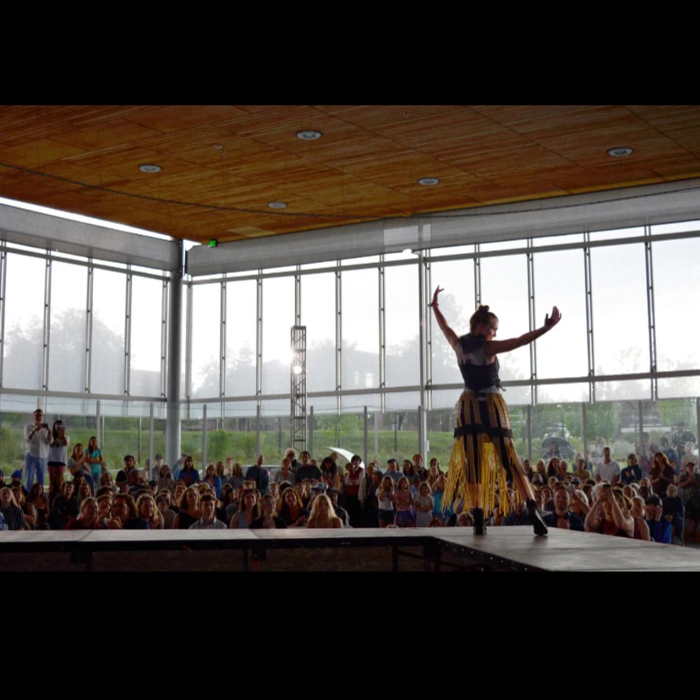 A model on stage in the foreground with a crowd of people in the background of a window-paneled arena