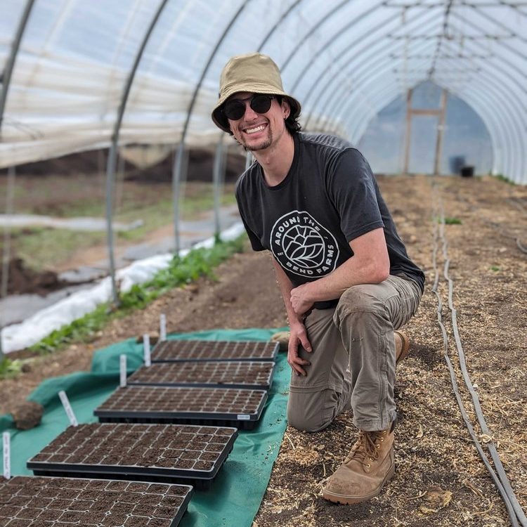 Young farmer with hat next to seeding trays in a greenhouse