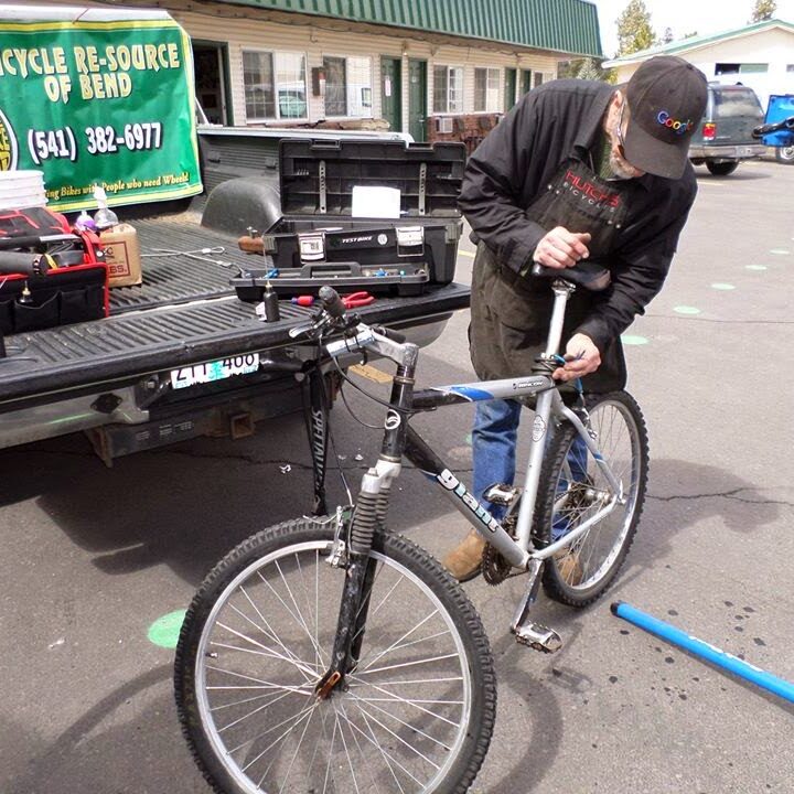 Person fixing a seat on a bicycle with a banner behind that reads Bicycle Re-Source of Bend