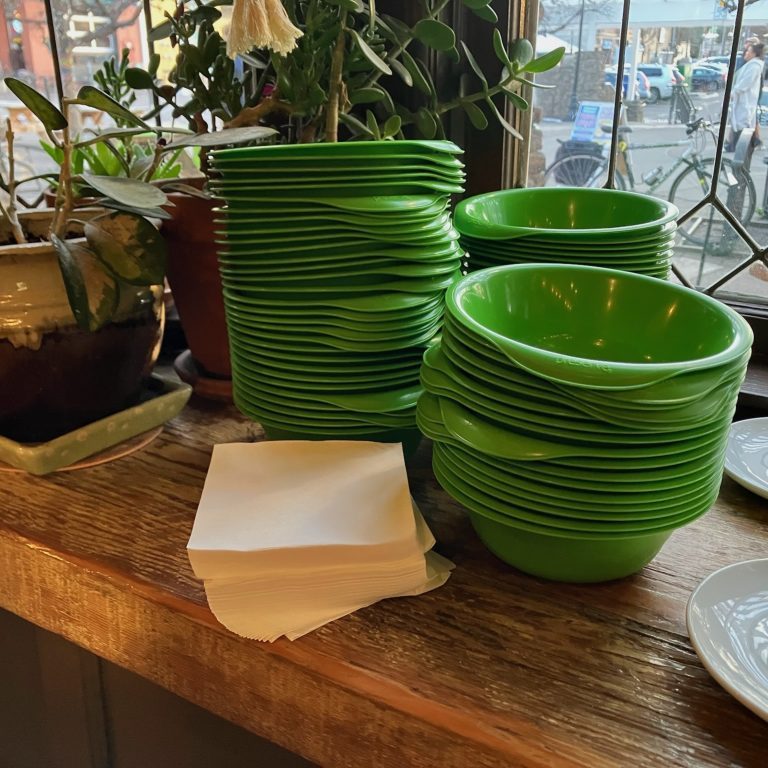 Stacks of green reusable plastic bowls on a wooden counter in front of a window