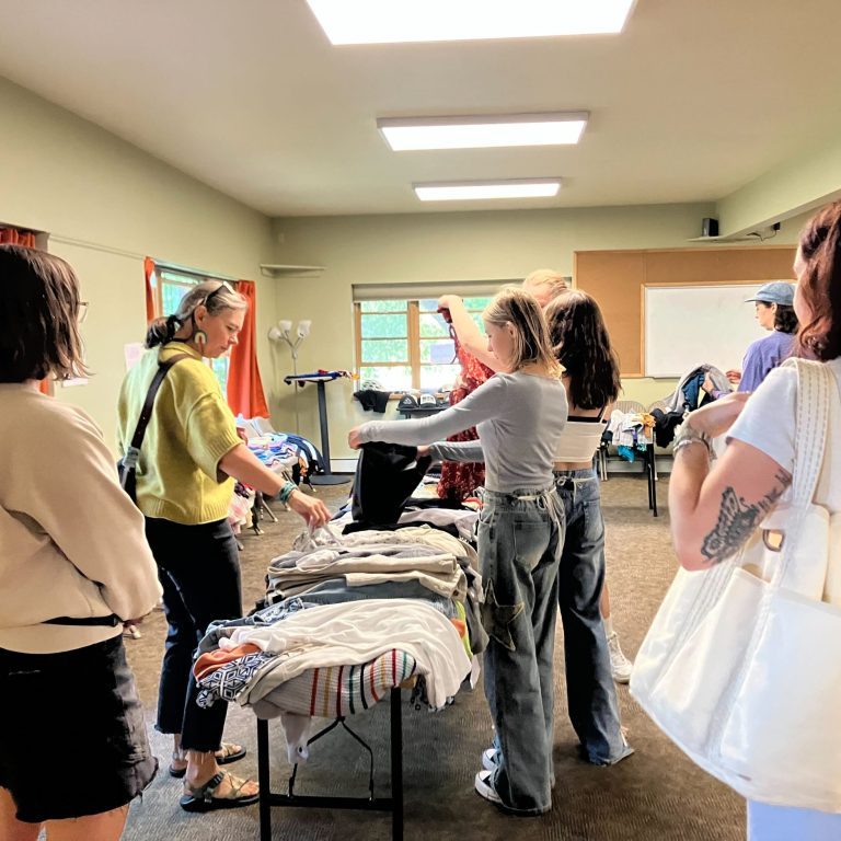 People sifting through piles of clothes organized on tables in a big room