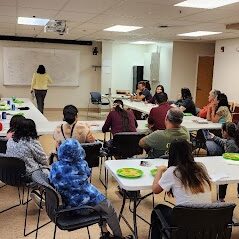 Youth and adults sitting at tables with green reusable plates in a community room