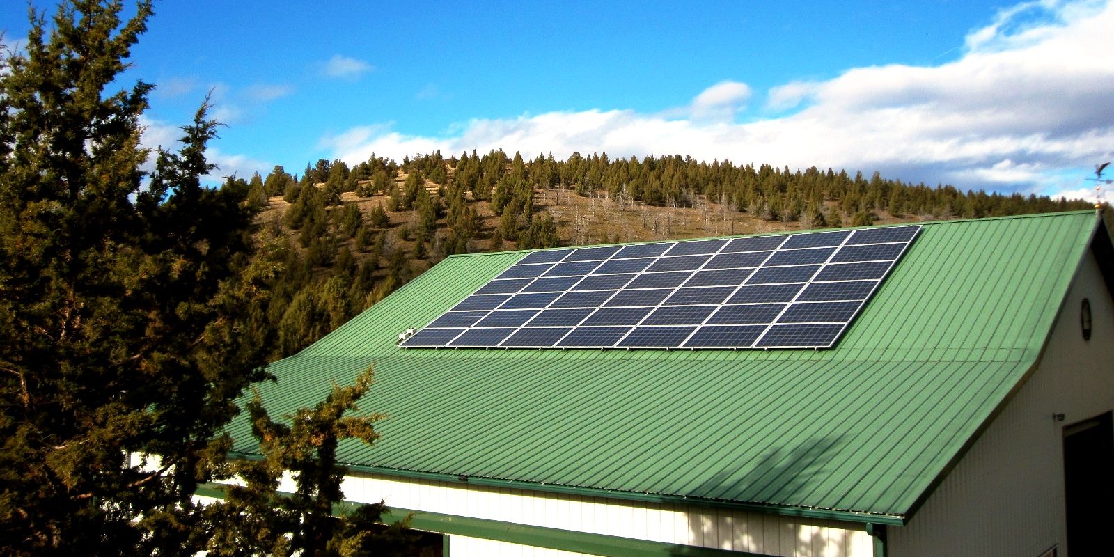A green rooftop of a shop building with solar panels on top and a hill in the background