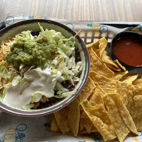 A tray of food featuring chips and salsa and mexican food in a ceramic reusable bowl